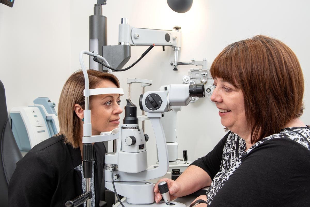 Woman getting an eye exam from a technician using a slit lamp in a clinic.
